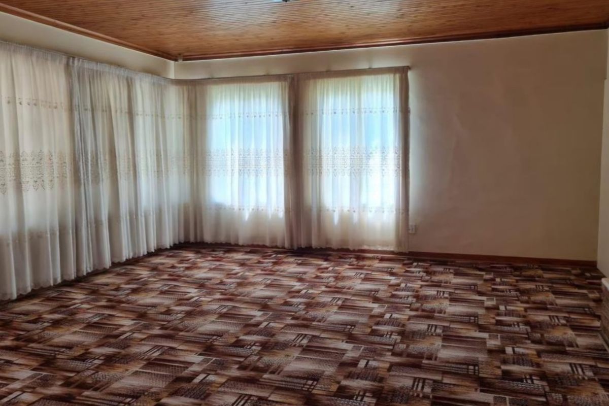 A spacious, empty living room featuring a timber-clad ceiling and patterned wall-to-wall carpeting, offering a blank canvas for renovation.