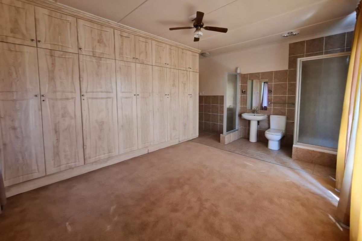 Spacious bedroom featuring extensive built-in cabinetry and an en-suite bathroom with a shower, pedestal basin, and toilet.