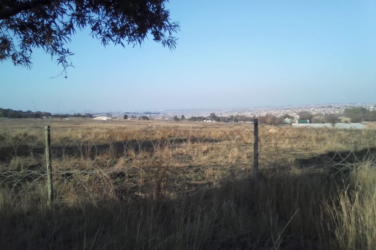 A wide-angle view of the vacant residential land featuring a perimeter barbed wire fence and distant urban landscape.