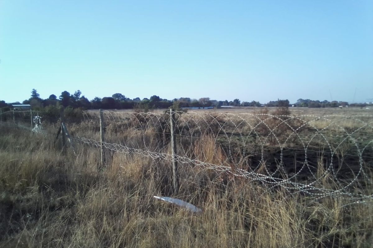 A view of a vacant residential plot featuring dry grass and perimeter fencing with razor wire.