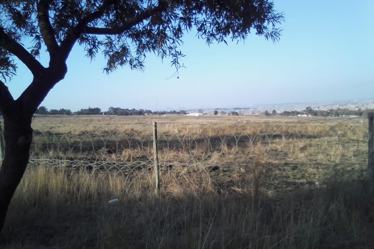 A view of a vacant residential plot featuring dry grass and a secure perimeter fence with razor wire.