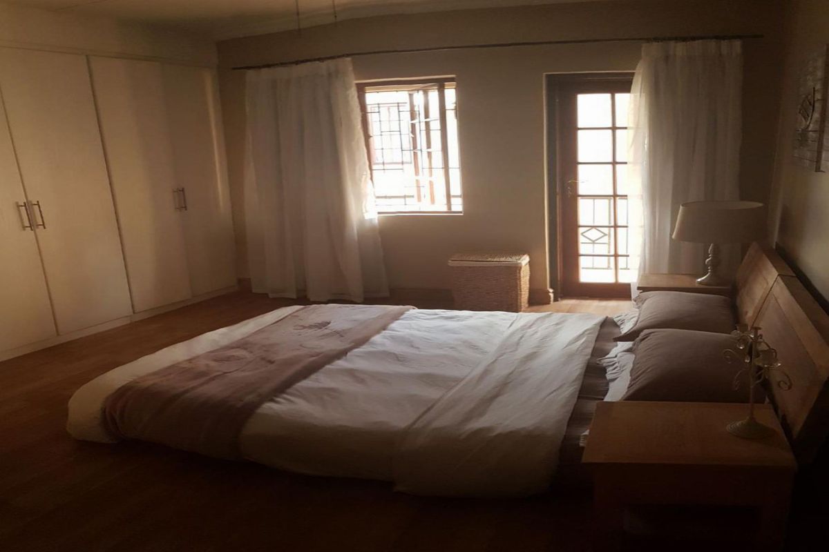 A bedroom featuring built-in cupboards, laminate flooring, and direct access to an outdoor area through a glass panel door.
