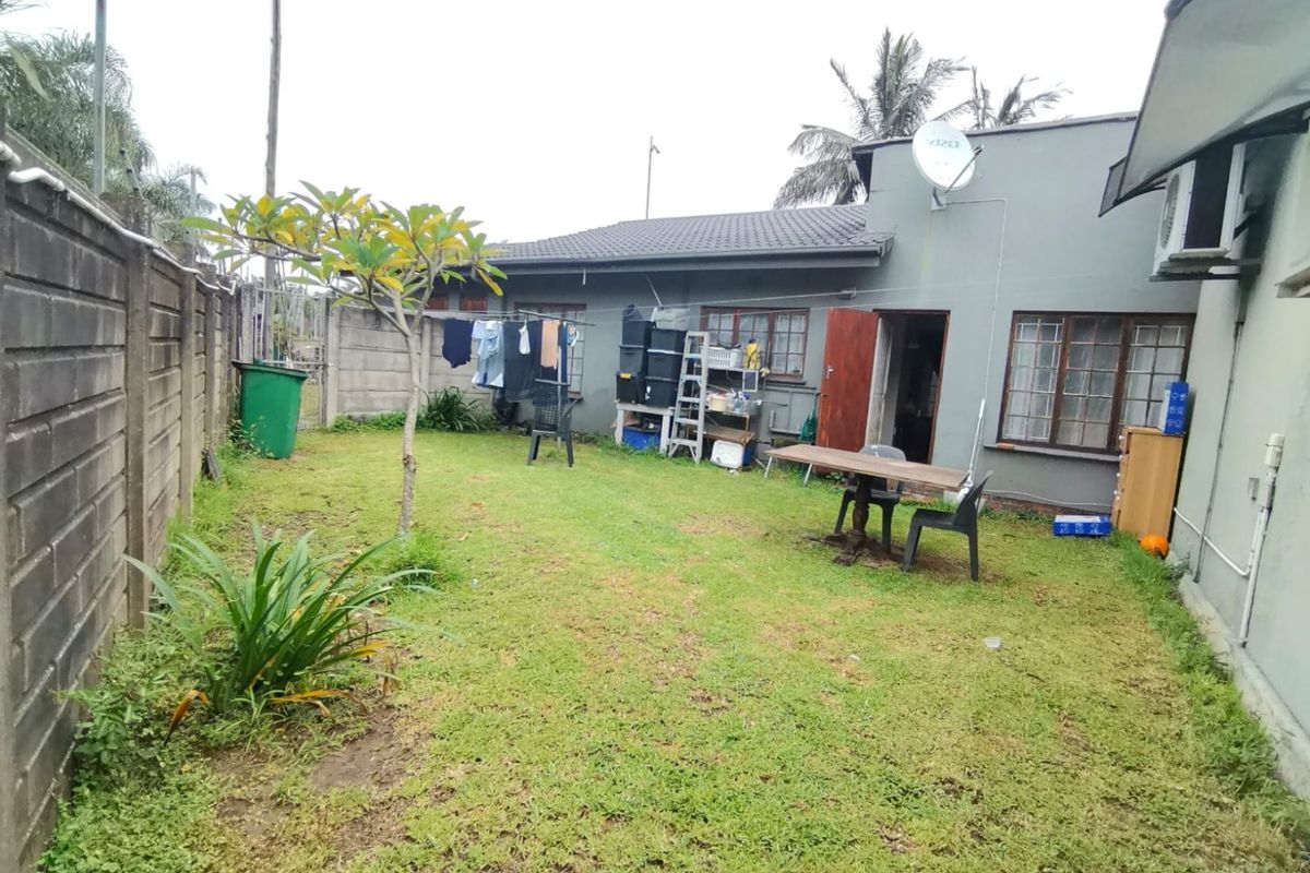 Rear garden area of the townhouse featuring a lawn, concrete boundary wall, and exterior access to the main dwelling.