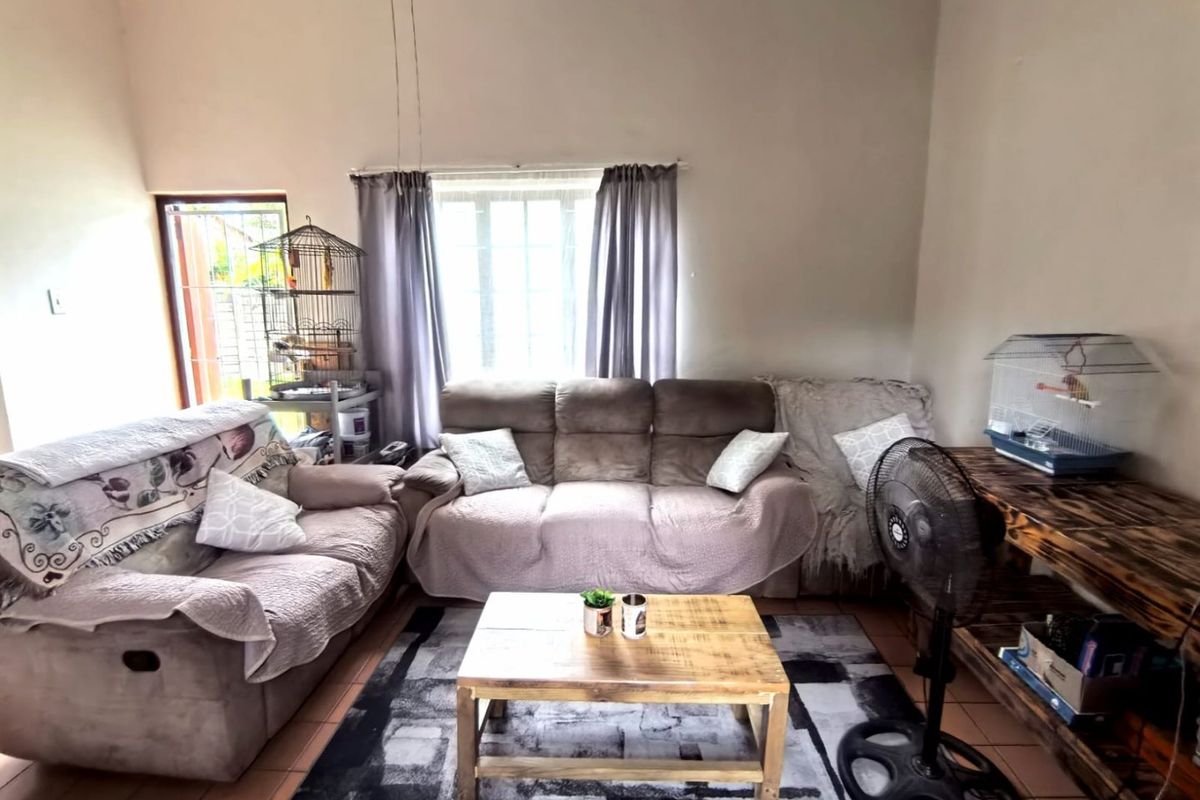 A living room featuring tiled flooring and a window with security bars, providing a functional space for relaxation.