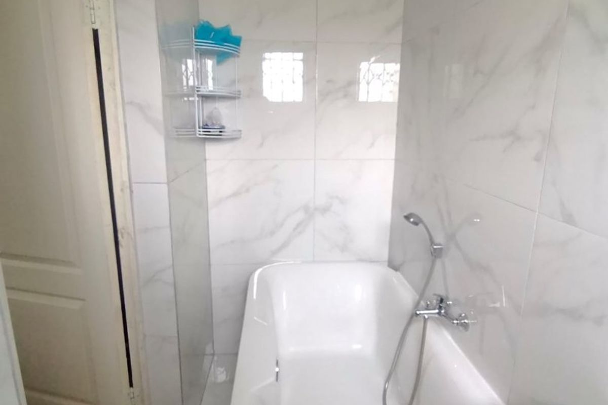 A compact bathroom featuring a bathtub with a handheld shower mixer and modern marble-look wall tiling.