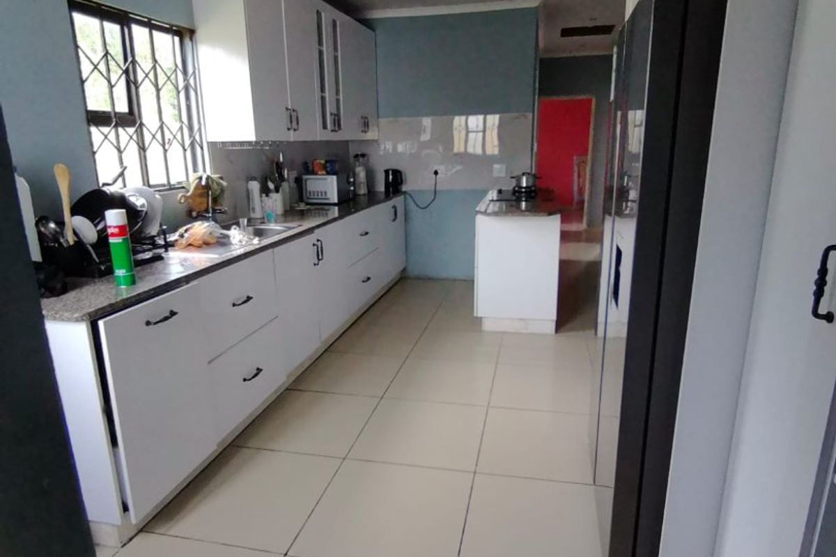 A functional kitchen featuring white built-in cabinetry, granite countertops, tiled flooring, and a window with security bars.
