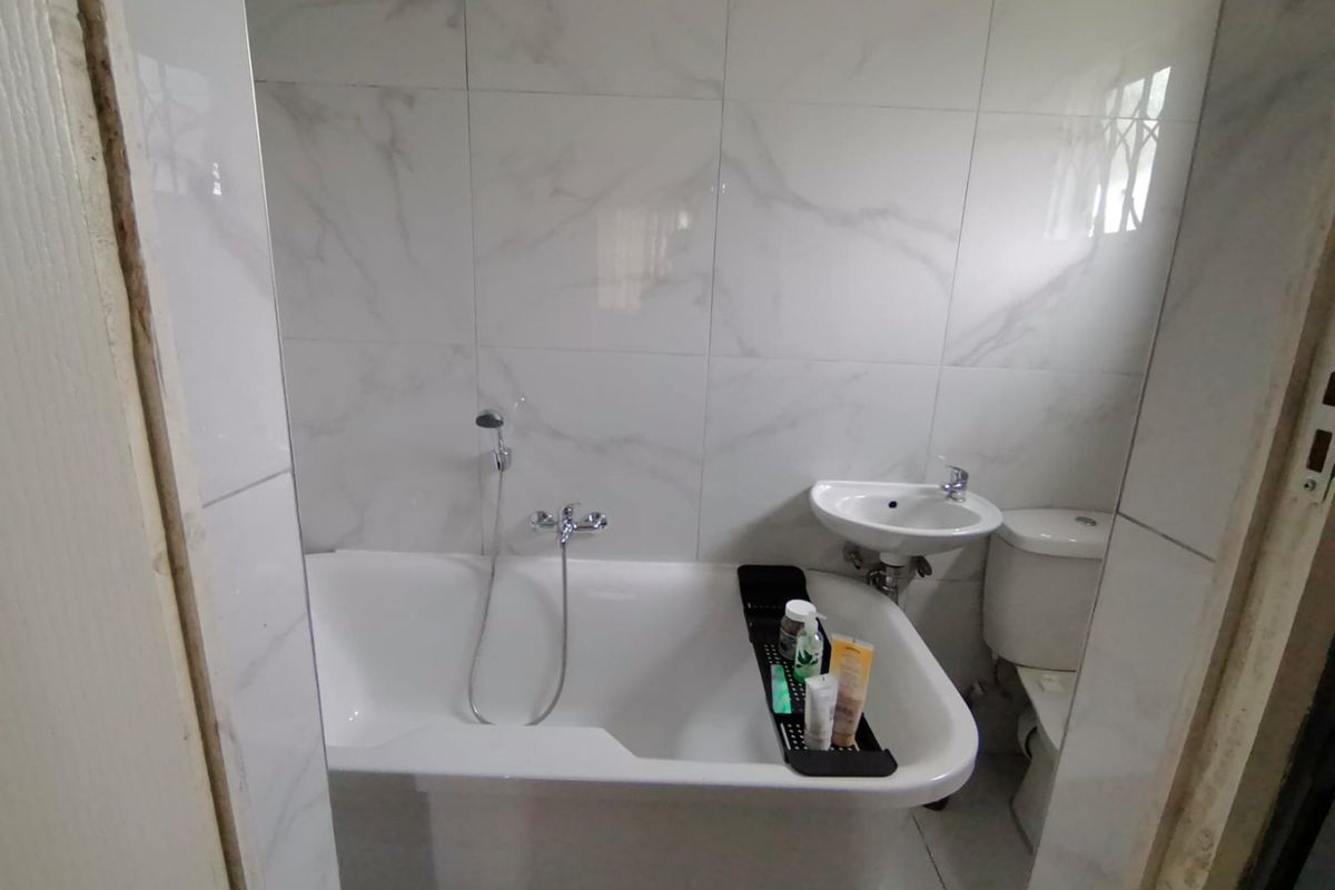 A compact bathroom featuring marble-look wall tiles, a bathtub with a handheld shower mixer, a wall-mounted basin, and a toilet.