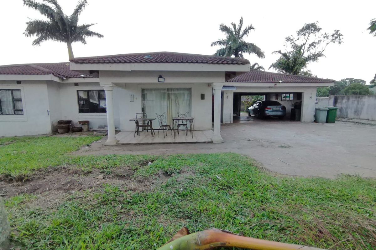 Rear view of the house featuring a covered patio, tiled roof, concrete driveway, and an integrated double garage with a spacious garden area.