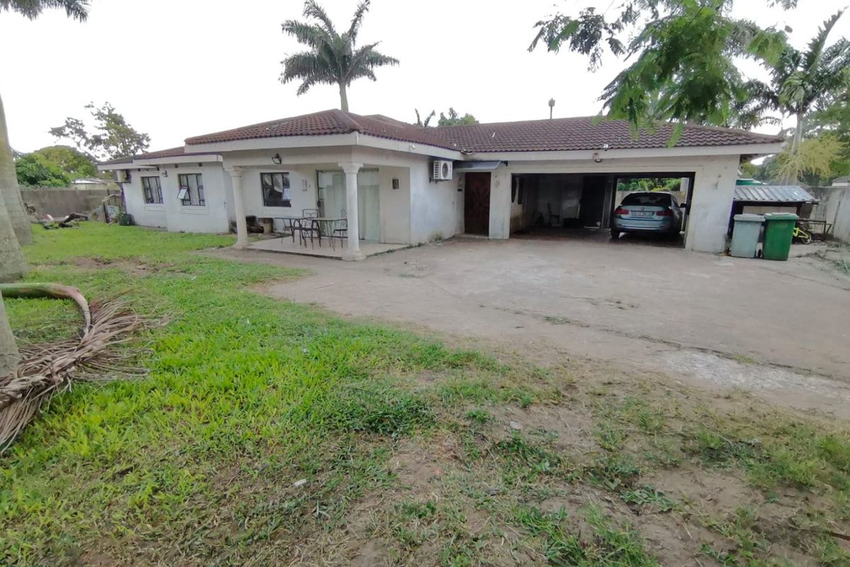 Rear view of a single-story house featuring a tiled roof, covered patio area, and an integrated double garage with a concrete driveway.