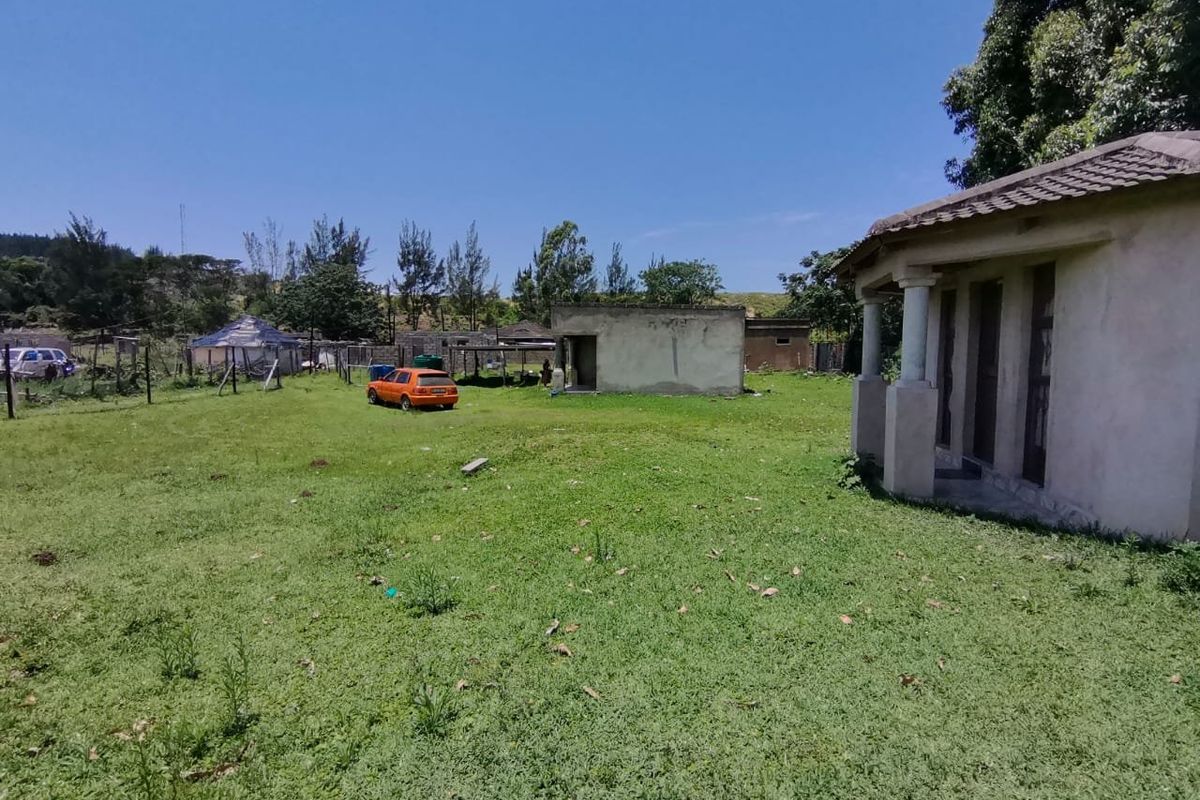 A spacious outdoor garden area featuring a small outbuilding, concrete columns, and perimeter fencing on a large plot of land.