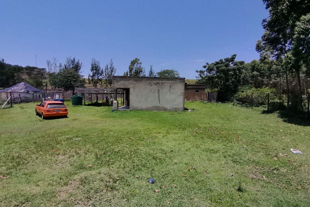 A view of the rear yard featuring a detached concrete structure, open lawn space, and perimeter fencing.