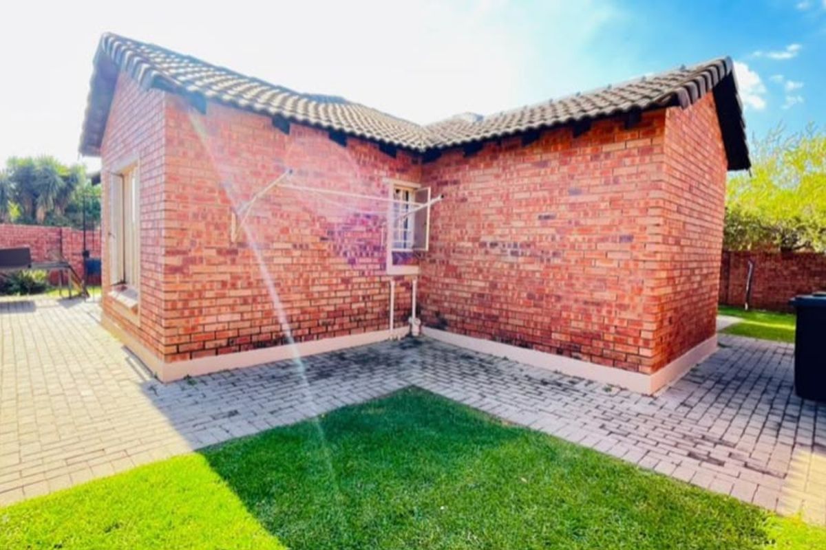 Rear view of the townhouse featuring face brick construction, a tiled roof, a paved courtyard area, and a small private lawn.