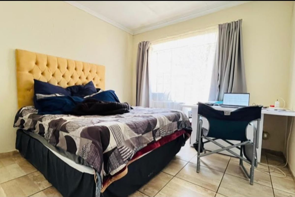 A functional bedroom featuring tiled flooring and large windows with curtain rails, providing a neutral base for personalization.