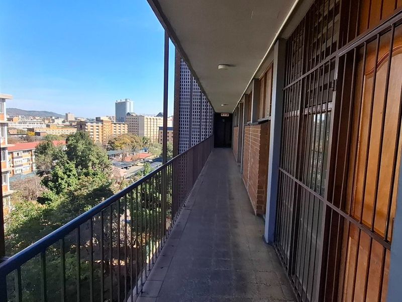An open-air apartment balcony featuring metal security gates, railings, and views of the surrounding urban landscape.