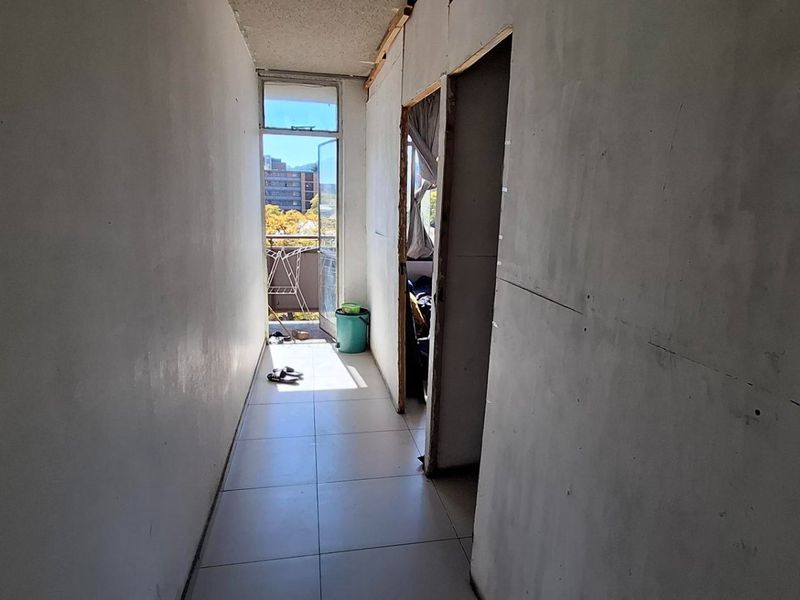 A narrow hallway in need of renovation, featuring unfinished wall surfaces and exposed ceiling edges, leading to an outdoor balcony area.