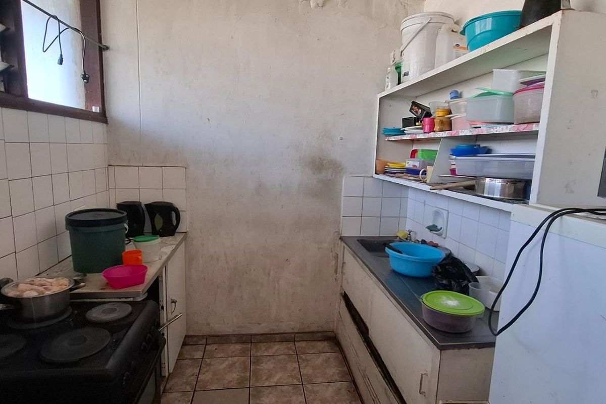 A compact kitchen featuring tiled splashbacks, a stainless steel sink, and built-in shelving, currently requiring cosmetic updates and wall repairs.
