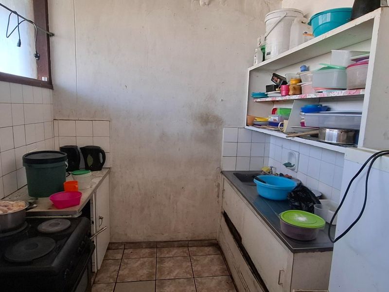 A compact kitchen featuring tiled splashbacks, a stainless steel sink, and built-in shelving, currently requiring cosmetic updates and wall repairs.