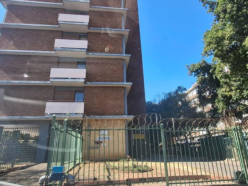 Exterior view of a multi-story brick apartment building featuring private balconies and secure perimeter fencing with razor wire.