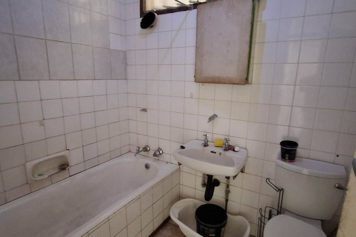 A dated bathroom featuring a standard bathtub, wall-mounted basin, and toilet with white tiled walls requiring renovation and modernization.