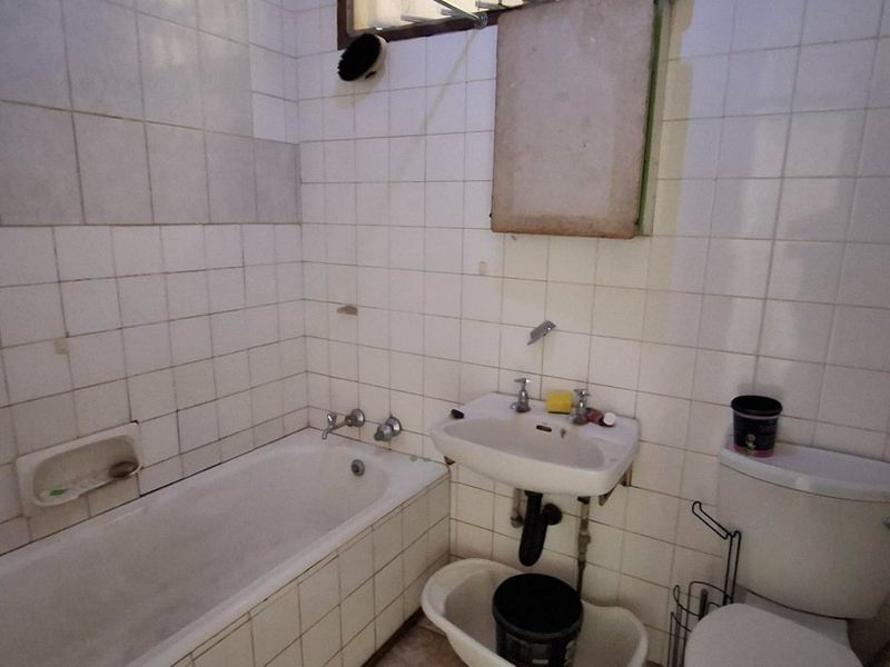 A dated bathroom featuring a standard bathtub, wall-mounted basin, and toilet with white tiled walls requiring renovation and modernization.