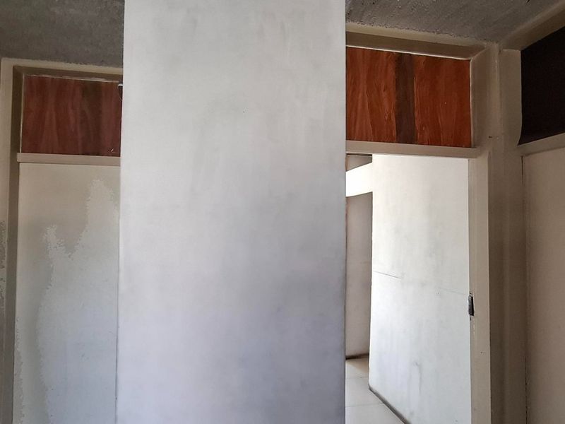 A vacant hallway area featuring internal doors and transom windows, currently requiring cosmetic updates and wall refinishing.