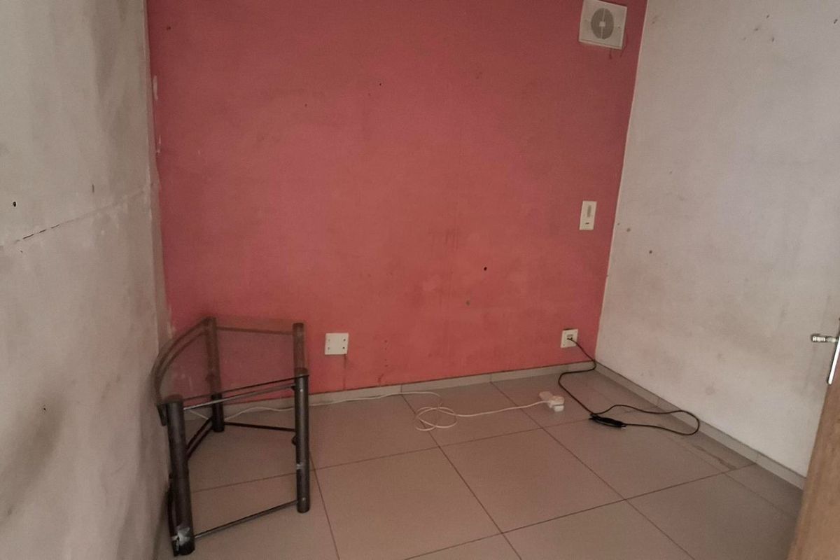 A small, empty bedroom featuring tiled flooring and an extractor fan, currently requiring wall repairs and fresh paint to improve its condition.
