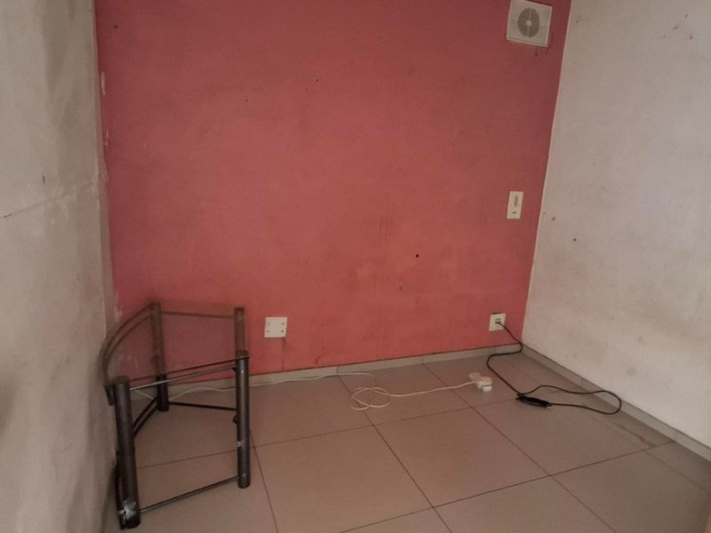 A small, empty bedroom featuring tiled flooring and an extractor fan, currently requiring wall repairs and fresh paint to improve its condition.