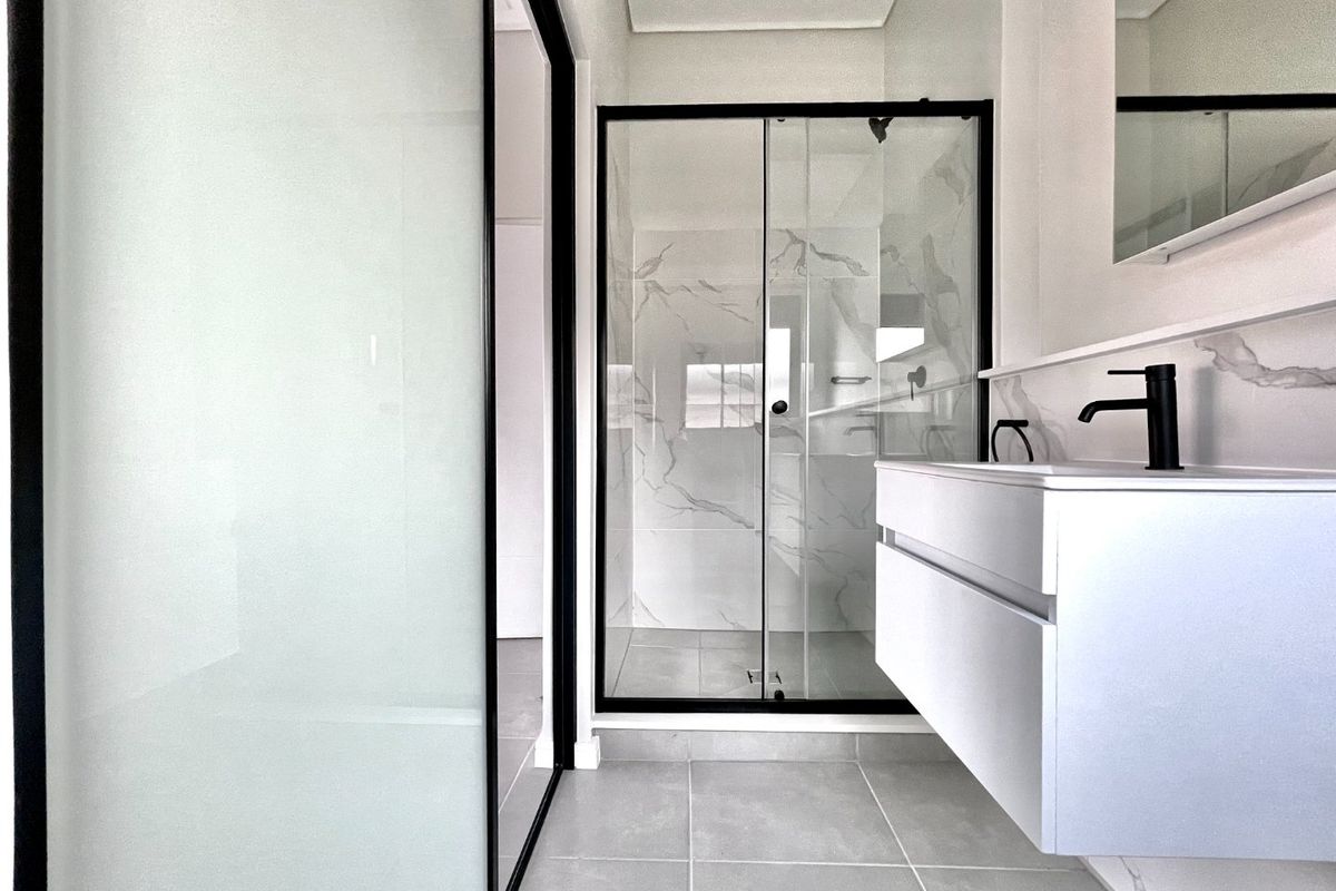 Modern bathroom featuring a floating vanity, black fixtures, and a glass-enclosed shower with marble-look wall tiling.