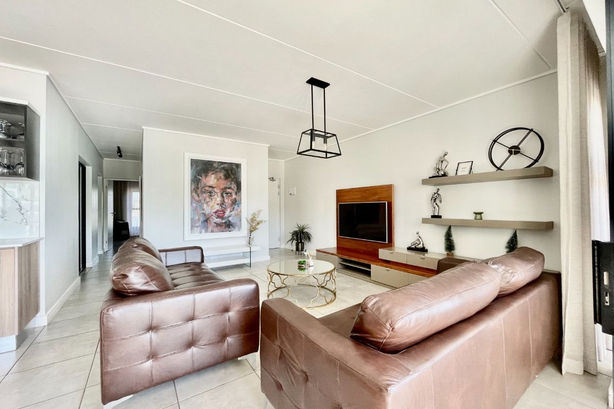 A well-maintained living room featuring tiled flooring, a built-in media console, floating wall shelves, and modern pendant lighting.