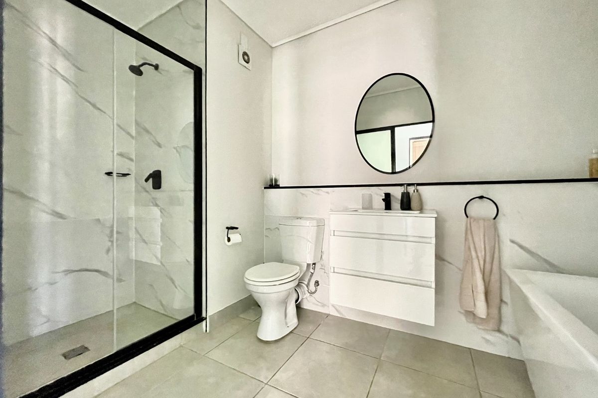Modern bathroom featuring a walk-in shower with black-framed glass, a wall-mounted vanity, a bathtub, and elegant marble-effect wall tiling.