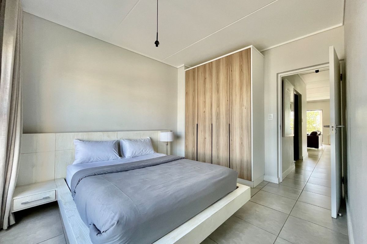 A modern bedroom featuring neutral tones, tiled flooring, and a large built-in wardrobe with wood-grain finish.