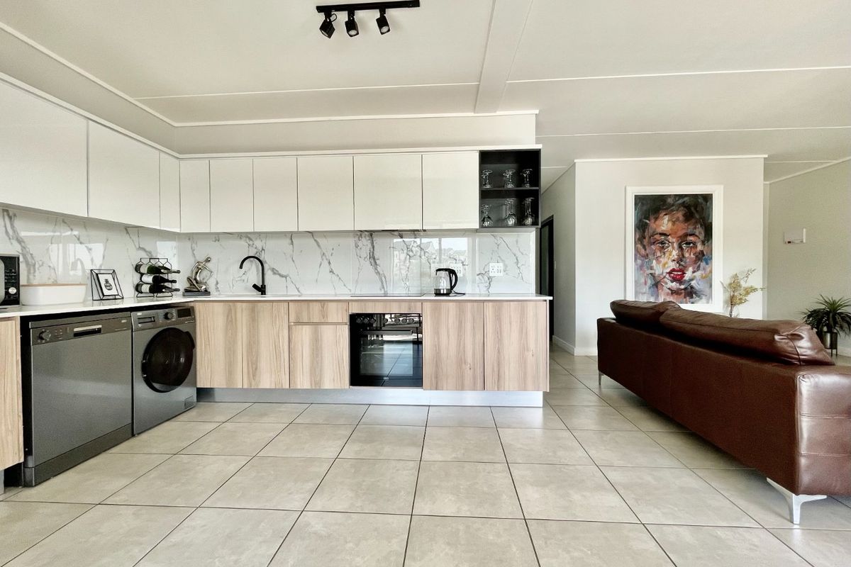 Modern open-plan kitchen featuring sleek two-tone cabinetry, marble-look splashback, integrated oven, and high-quality ceramic floor tiles in a bright, contemporary living space.
