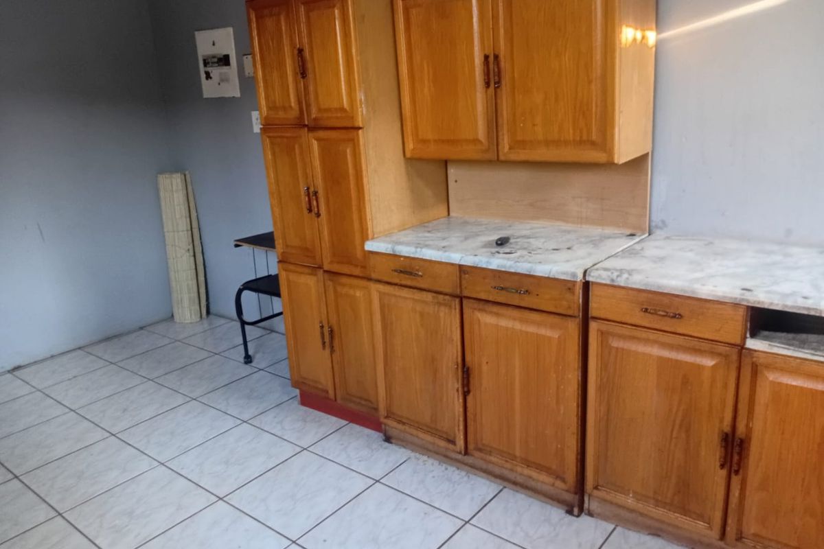 A functional kitchen area featuring wooden cabinetry, laminate countertops, and ceramic floor tiles, offering a blank canvas for potential renovation and modernization.