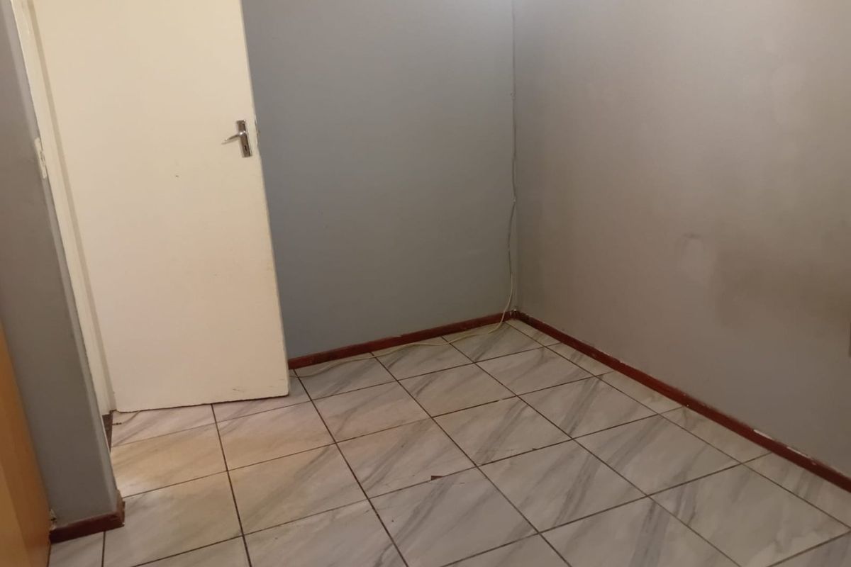 An empty bedroom featuring tiled flooring and grey painted walls, requiring minor cosmetic updates and repairs to wall surfaces.