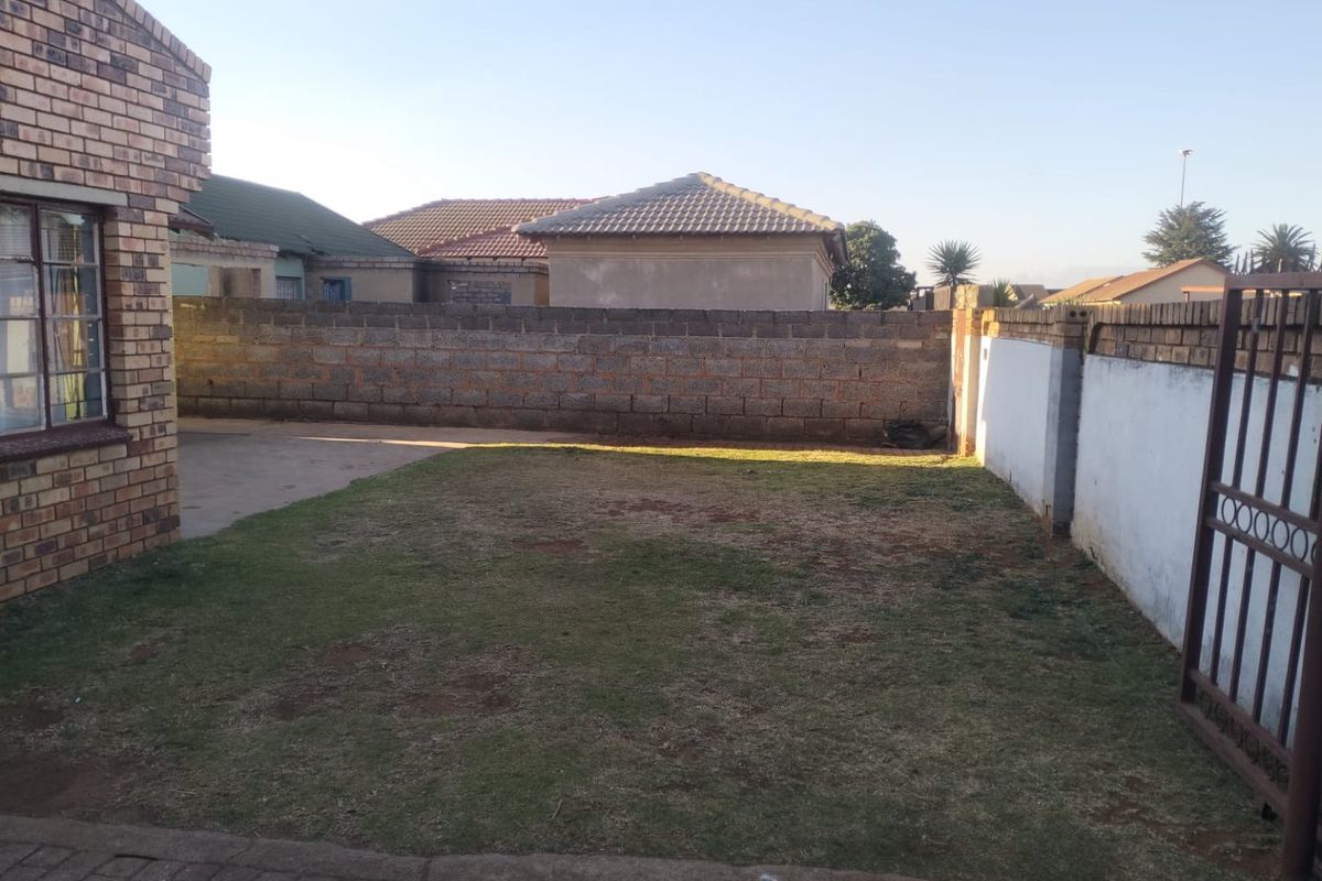 A private rear garden area featuring a lawn, concrete paving, and secure brick boundary walls with a metal access gate.