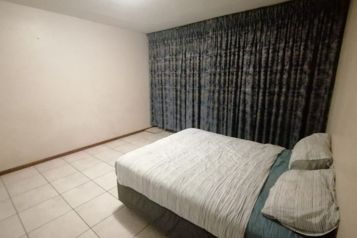 A simple bedroom featuring tiled flooring and full-length curtains covering the window area.