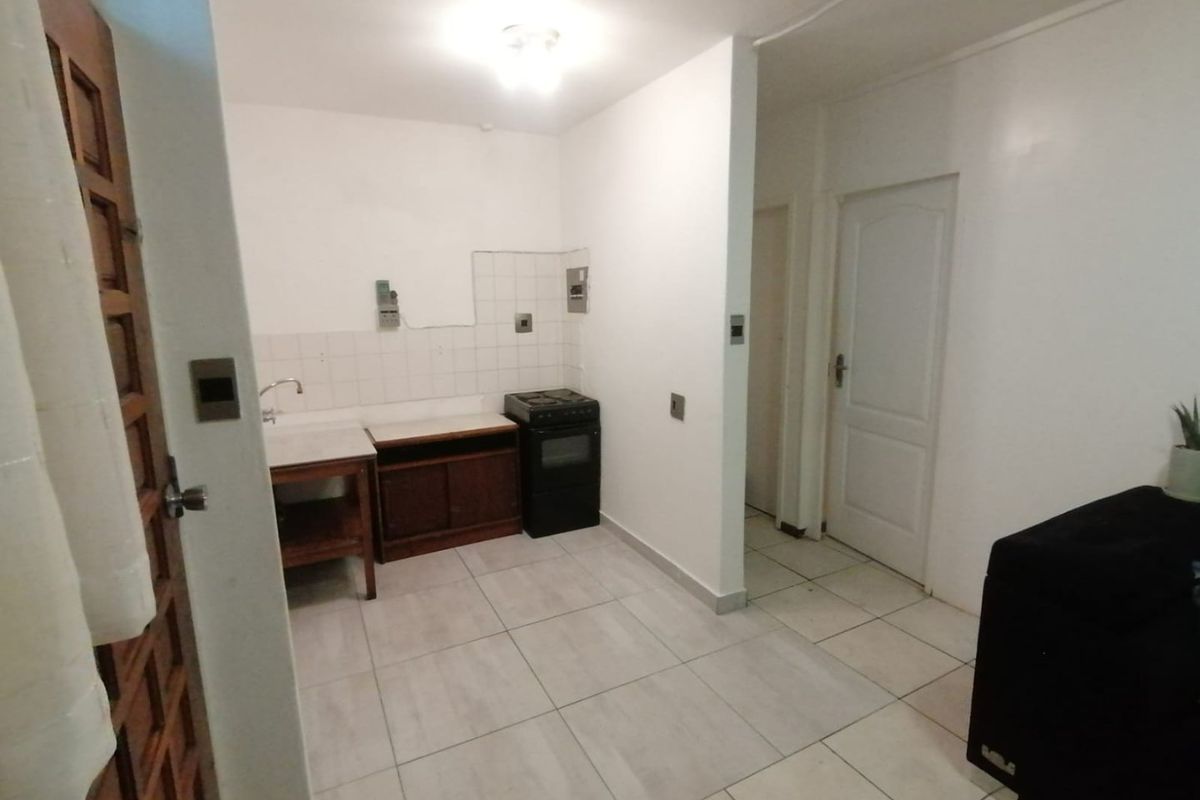 A compact kitchen area featuring tiled flooring, a basic sink unit, and a freestanding stove, requiring cosmetic updates to improve functionality and aesthetic appeal.
