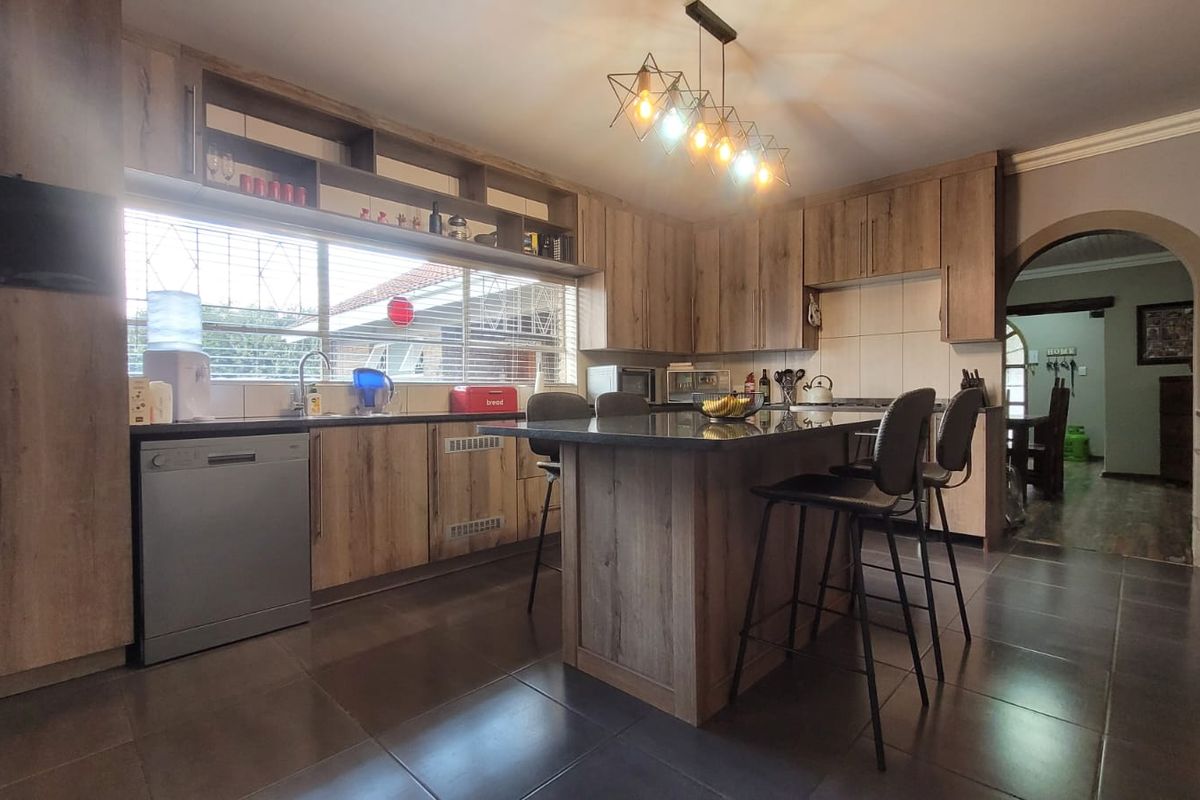 Modern kitchen featuring wood-finish cabinetry, a central island with stone countertops, tiled flooring, and an open-plan layout leading to an adjacent living area.