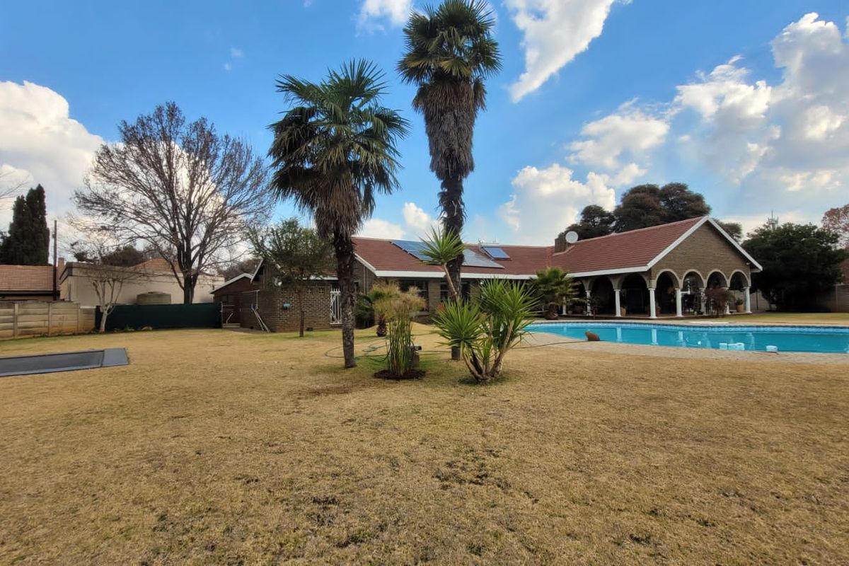 Spacious rear garden featuring a large swimming pool, a covered patio with arched columns, and a brick-faced house with solar panels.