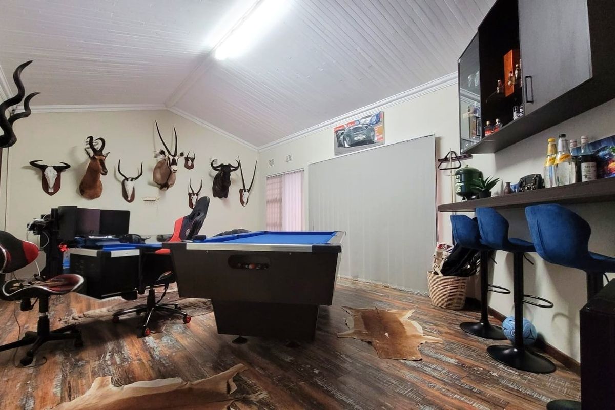 A spacious living area featuring vaulted ceilings, laminate flooring, and a built-in bar counter, currently utilized as a recreational and gaming space.