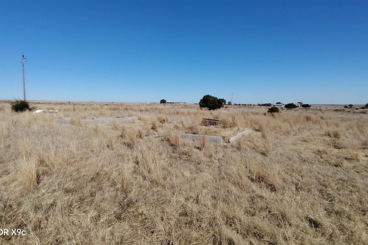 Open farm land featuring a concrete foundation remnant and utility pole, set within a vast, dry grass landscape.