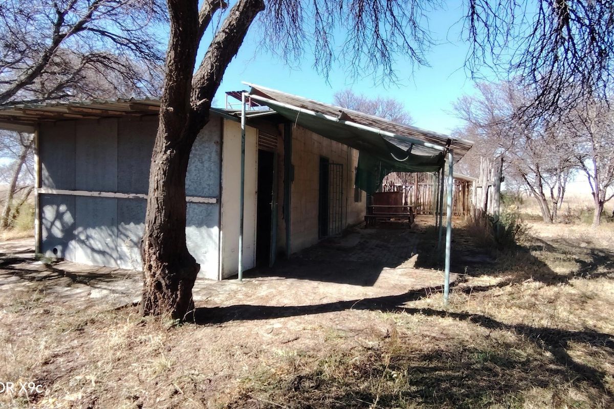 Rear view of a farm structure featuring a corrugated metal roof and a covered patio area in need of maintenance.