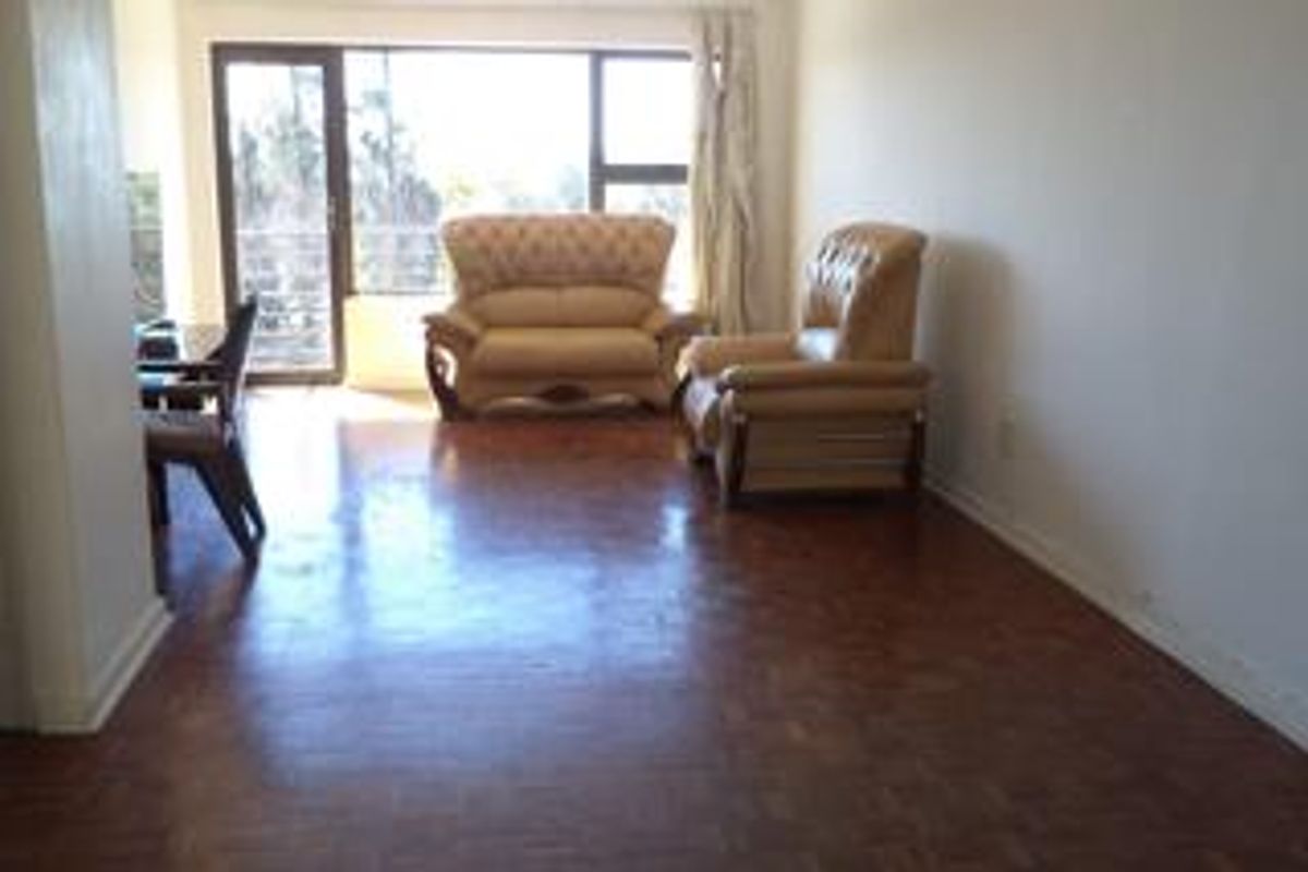 Spacious living area featuring classic parquet flooring and large sliding glass doors providing natural light and access to the balcony.