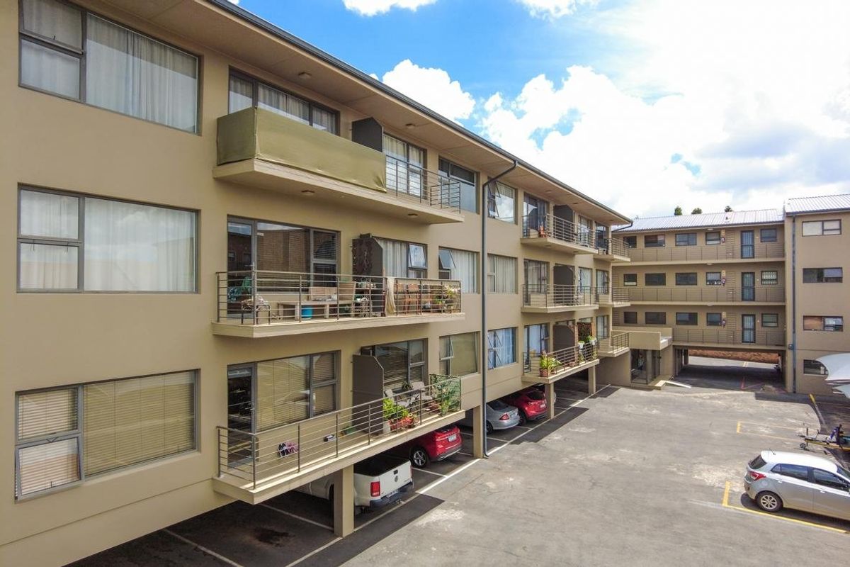 Exterior view of a multi-story apartment complex featuring private balconies, aluminium window frames, and an asphalt parking area.