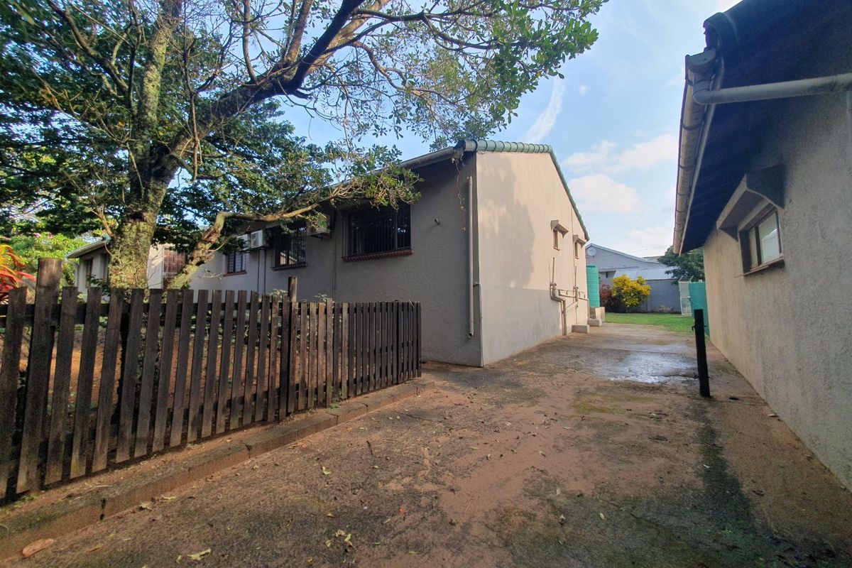 Rear exterior view of the property featuring a concrete driveway, timber fencing, and established trees alongside the building structure.