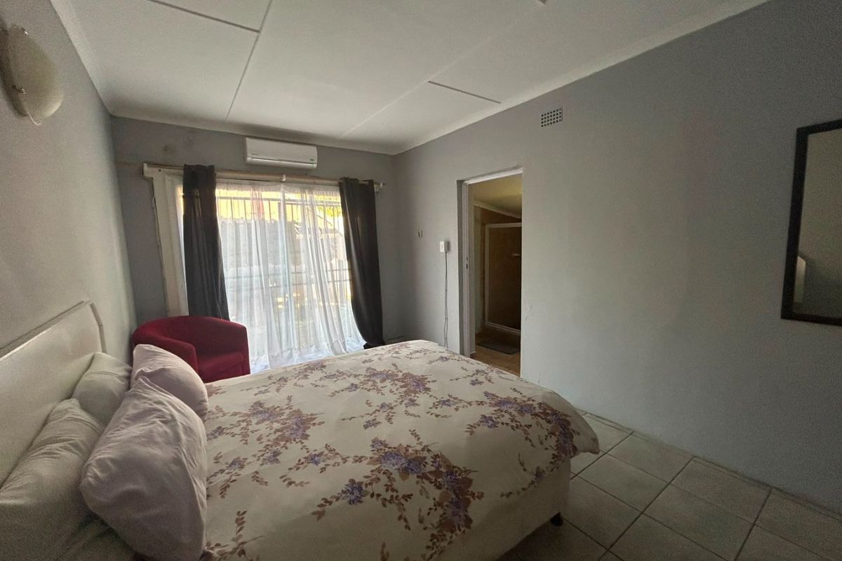A functional bedroom featuring tiled flooring, an integrated air conditioning unit, and direct access to an en-suite bathroom through a doorway.