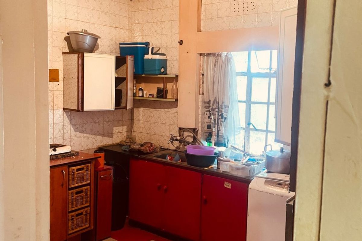 A compact kitchen featuring timber ceilings, tiled splashbacks, and red cabinetry, offering a functional layout in need of modernization.