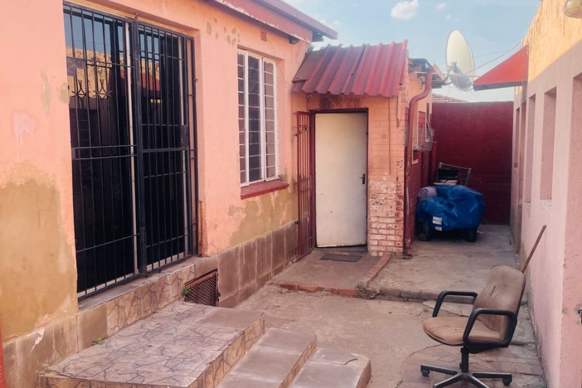 Rear exterior view of the property featuring a paved courtyard, tiled entrance steps, and security gates on the main access point.
