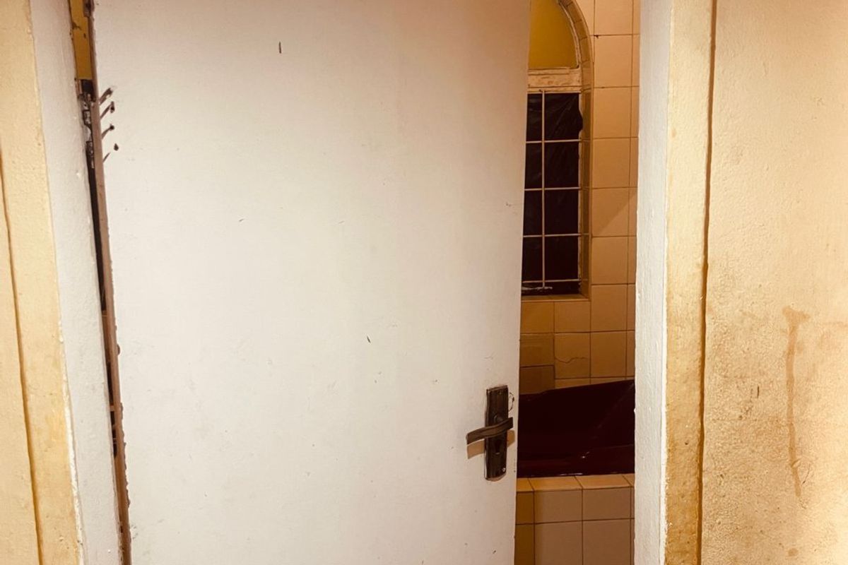 A view into a dated bathroom featuring tiled walls, a built-in bathtub, and an arched window, currently showing significant signs of wear and surface staining.