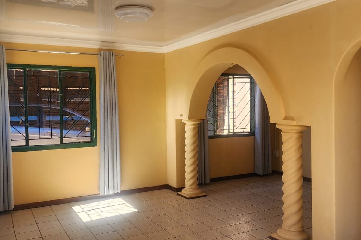 An empty living area featuring decorative archways with spiral columns, tiled flooring, and security bars on the windows.